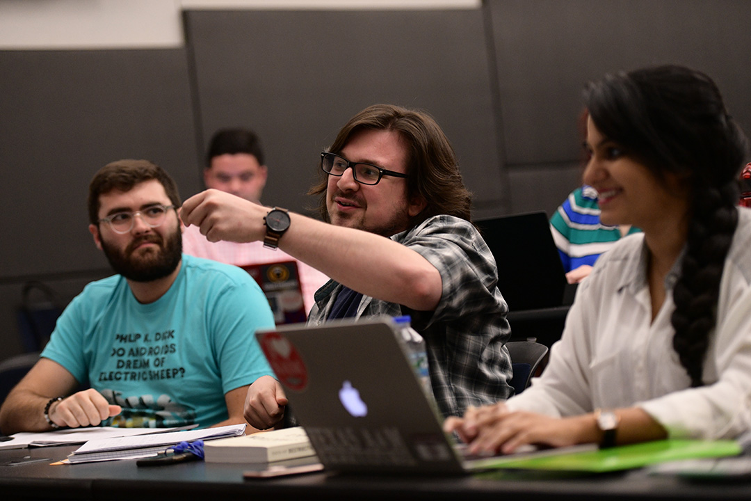 Three students in a classroom, with the middle student speaking and gesturing
