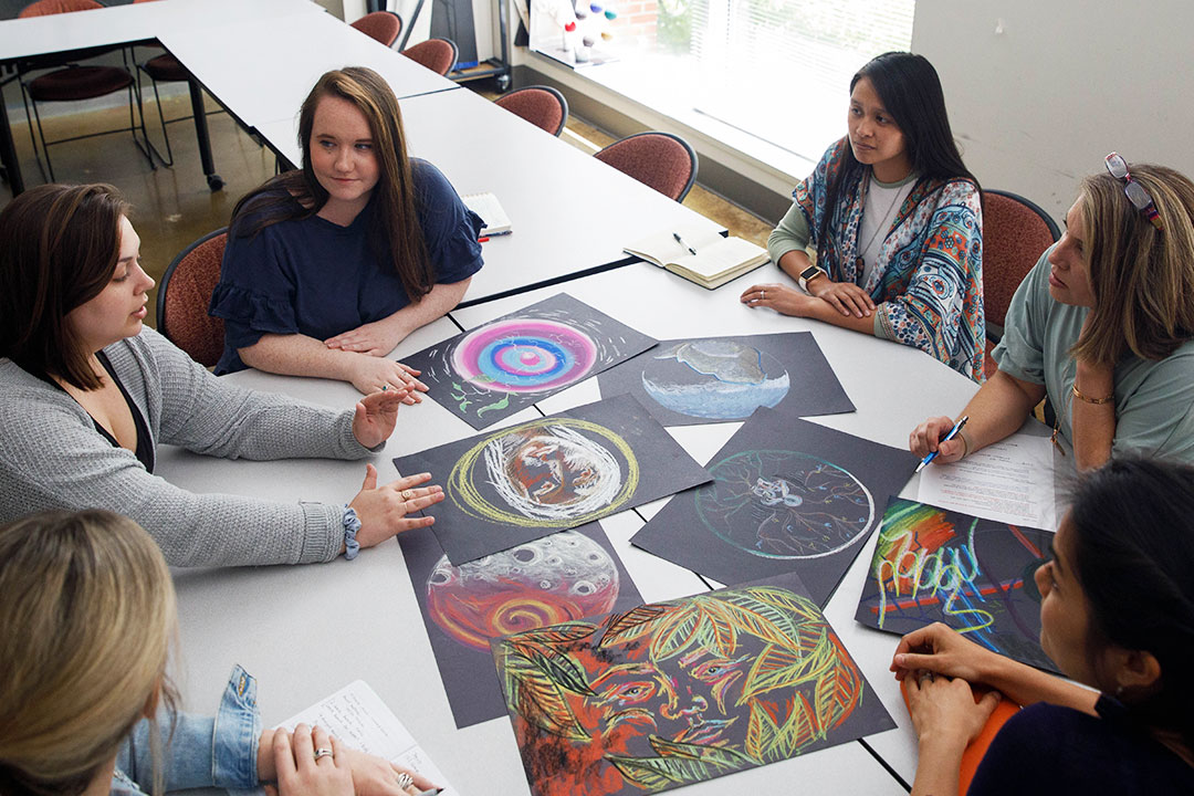 Art therapy students sitting in a circle discussing their artwork in class