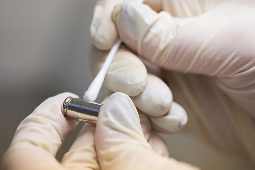 Close-up of someone in a forensics lab wearing gloves and working with a bullet casing